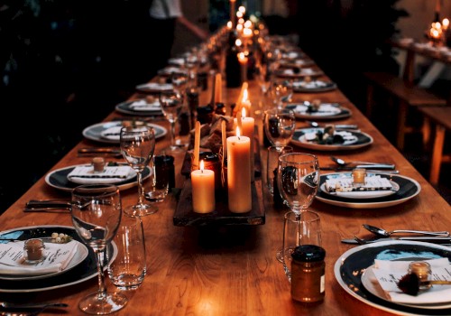 A long dining table is elegantly set with plates, cutlery, glasses, and lit candles, creating a warm, inviting atmosphere.
