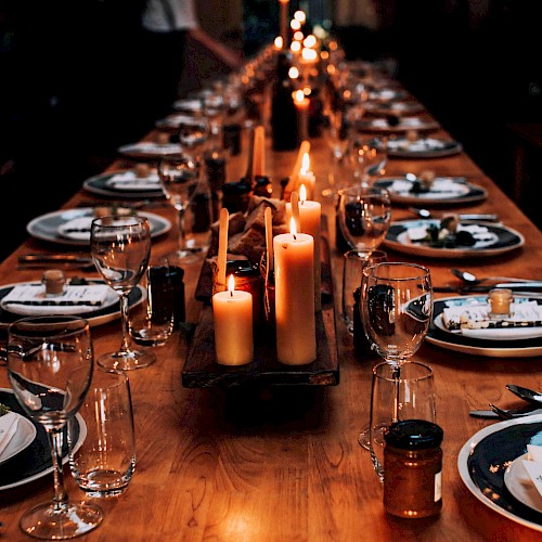 A long dining table is elegantly set with plates, cutlery, glasses, and lit candles, creating a warm, inviting atmosphere.