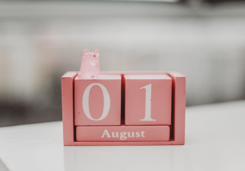 The image shows a pink desk calendar set to August 1, featuring a small pink hippopotamus figurine on top.