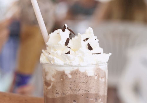 A chocolate frozen drink topped with whipped cream and chocolate shavings, served in a glass with a straw.