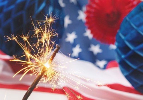 A lit sparkler in front of an American flag and festive decorations, creating a celebratory and patriotic scene.