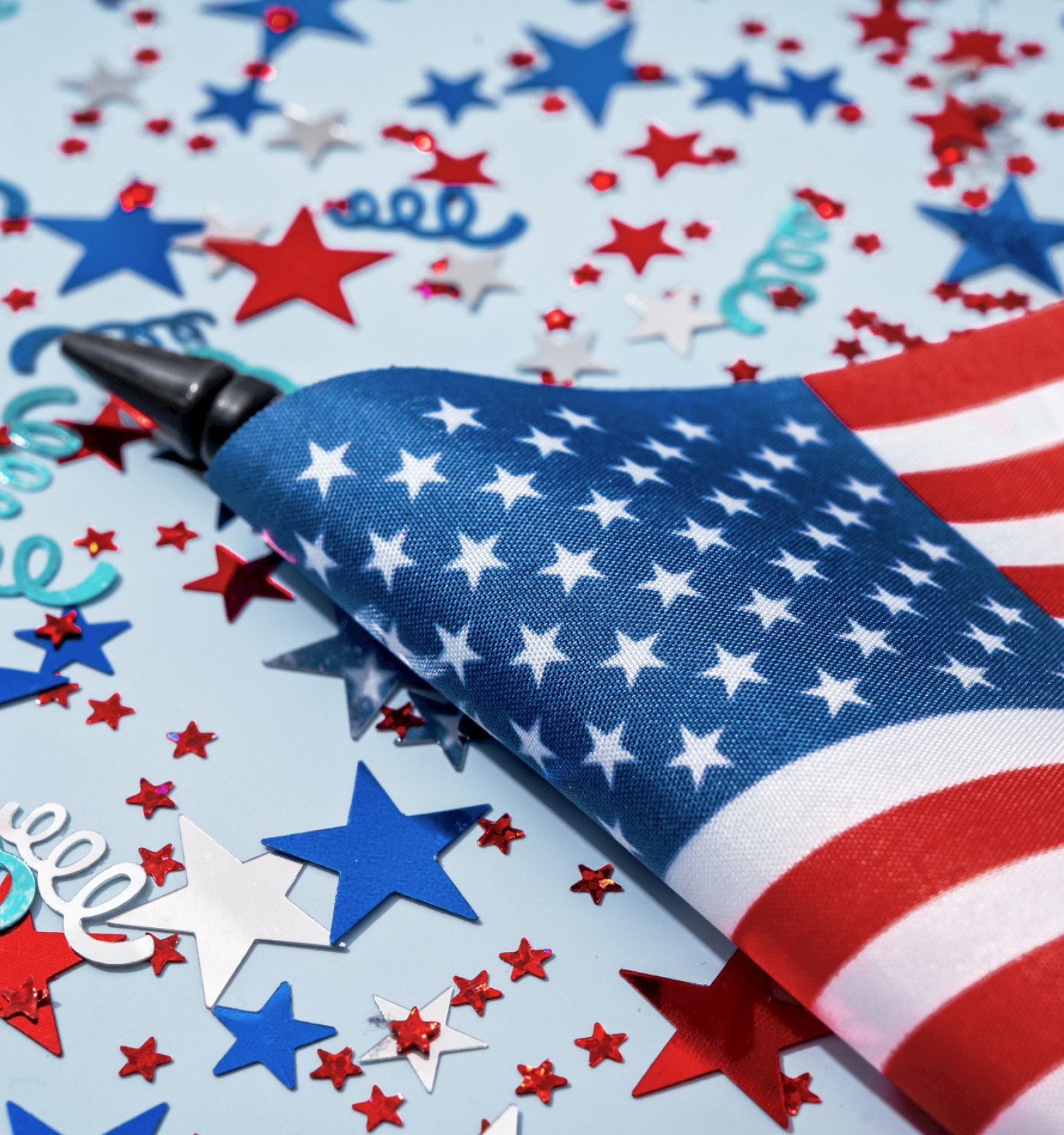 A small American flag surrounded by red, white, and blue star confetti on a light background.