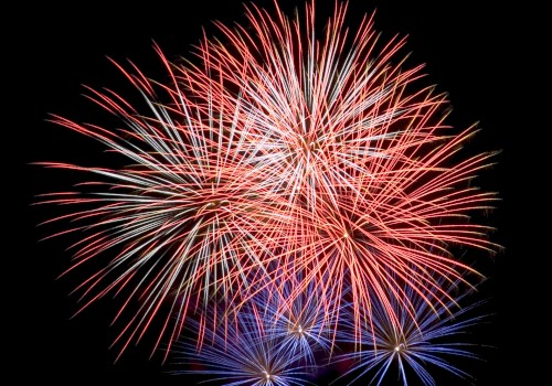 Fireworks explode in the night sky, displaying vibrant red and blue bursts.