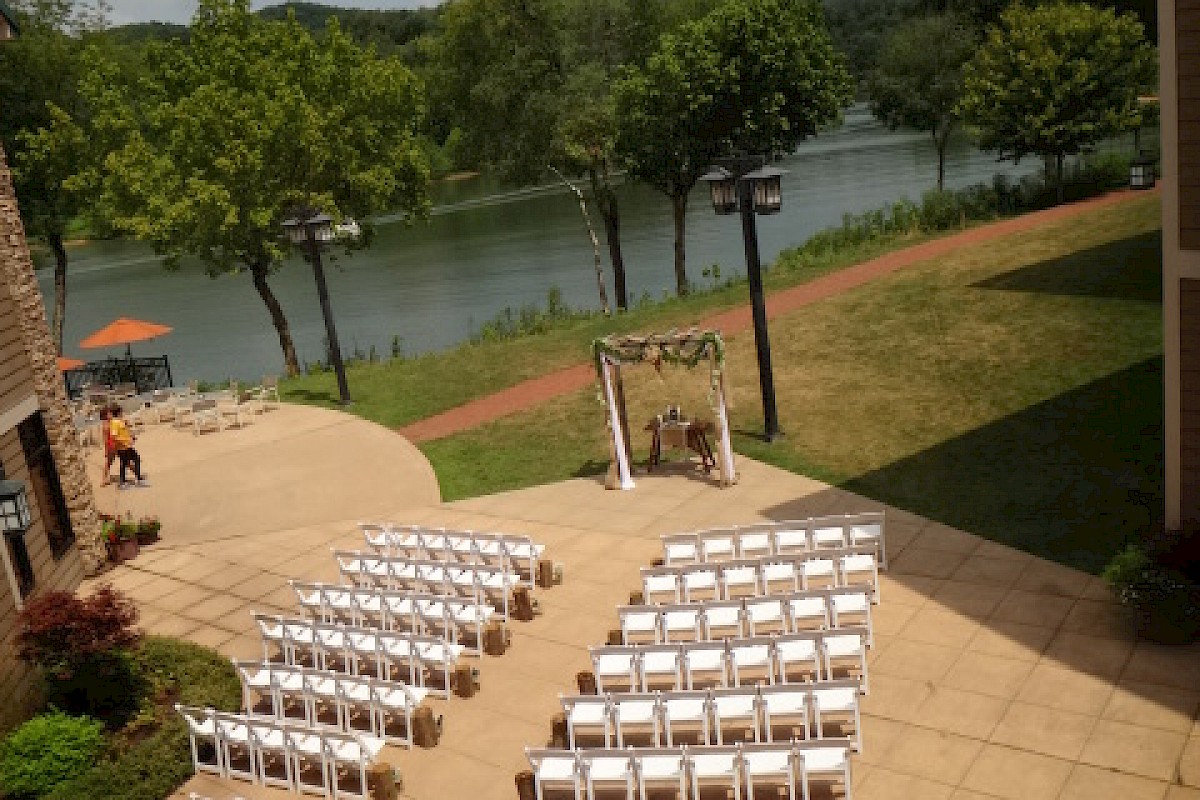 An outdoor wedding setup by a lake, featuring rows of white chairs facing a decorated arch under a partly cloudy sky.
