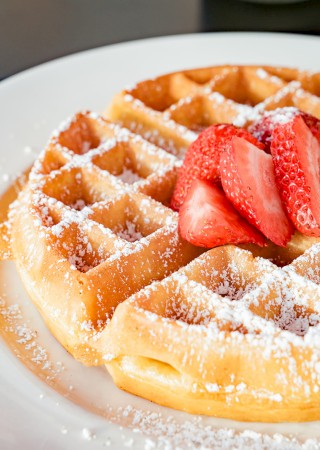 A plate of waffles topped with powdered sugar and fresh strawberry slices.