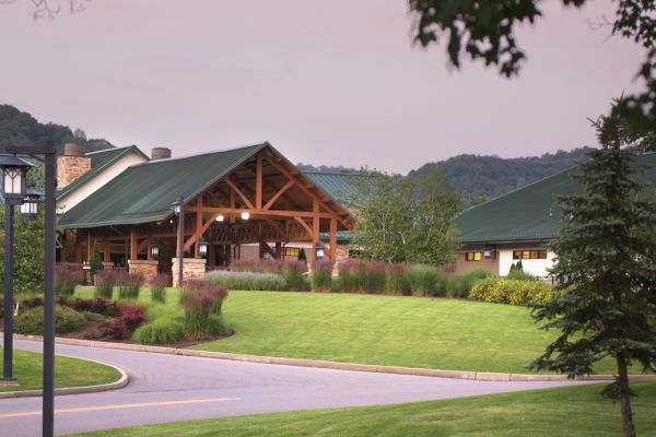 This image shows a scenic view of a building with a green roof, surrounded by a well-manicured lawn and trees, set against a backdrop of hills.
