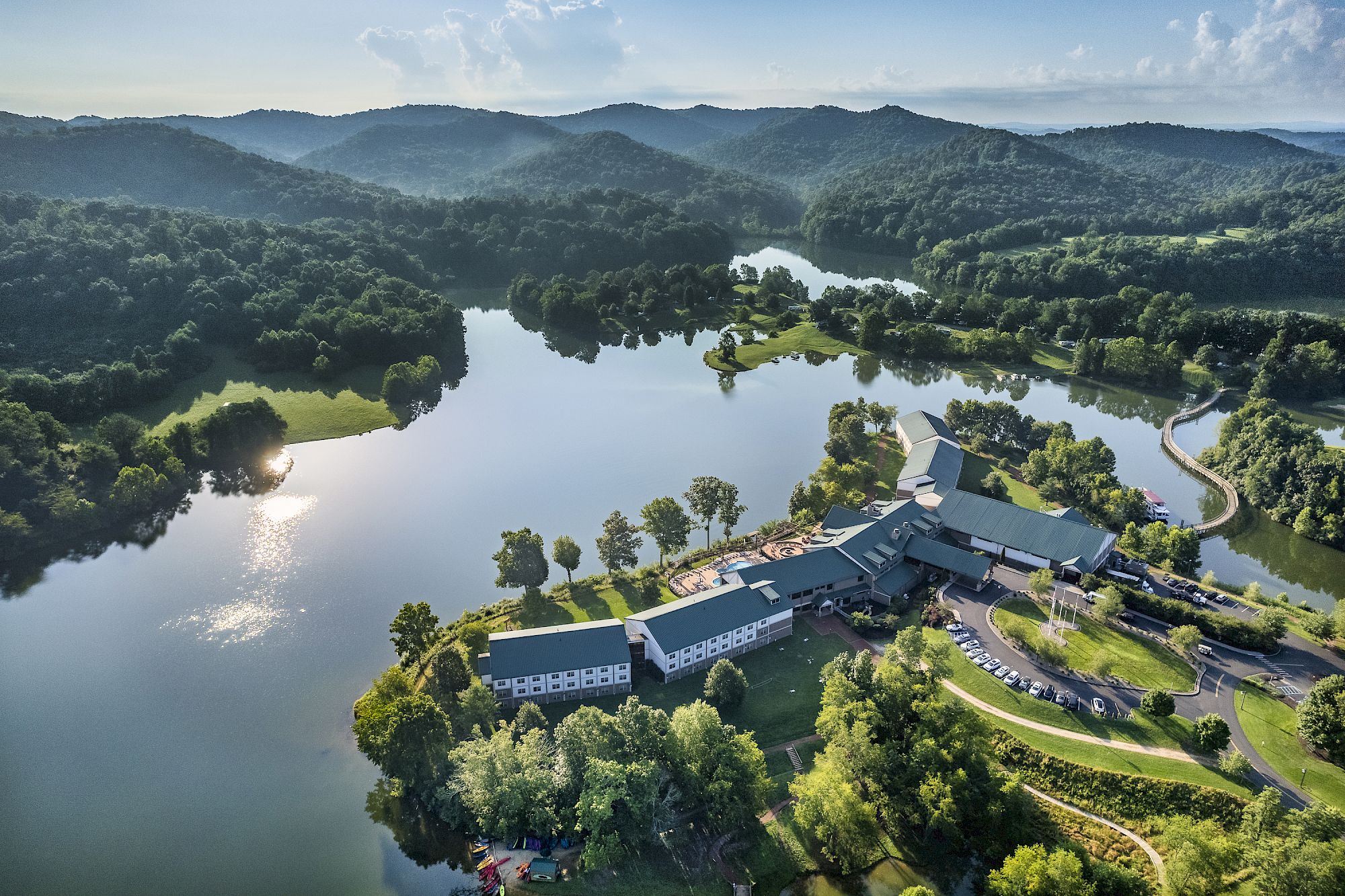 An aerial view of a large resort or estate surrounded by trees and lakes in a hilly area under a blue sky with scattered clouds.